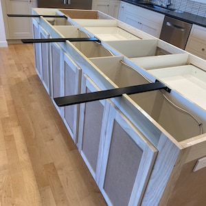 May include: A white kitchen island with black metal brackets supporting the countertop. The island has multiple drawers and cabinets.