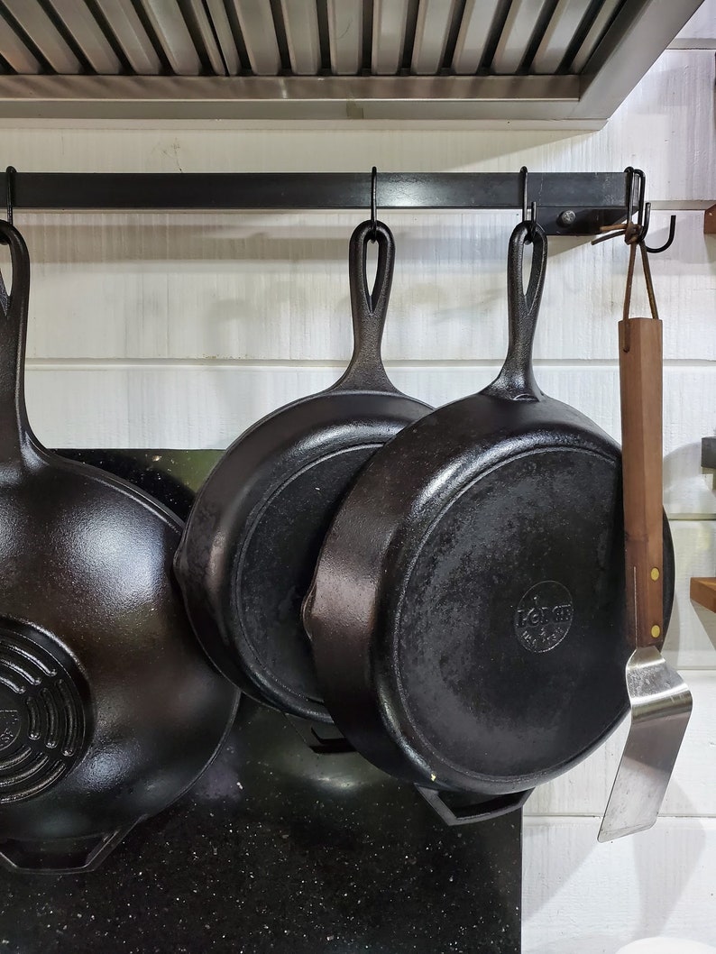Kitchen with metal utensil bar with hooks hold pots and pans with a white shiplap background.