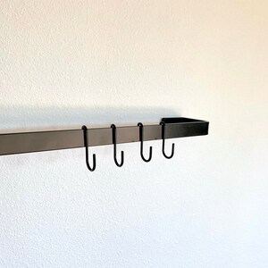 Black metal utensil bar mounted on white wall with hanging s hooks