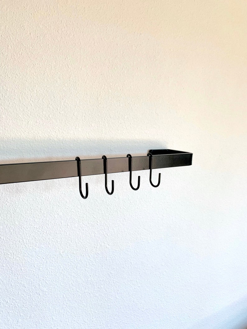 Black metal utensil bar mounted on white wall with hanging s hooks
