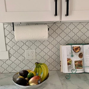 A white bright kitchen with a black paper towel holder mounted under white kitchen cabinets. Light gray countertops and tile backsplash.