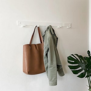 May include: White wall mounted coat rack with five hooks. A brown leather tote bag and a green jacket are hanging on the hooks.