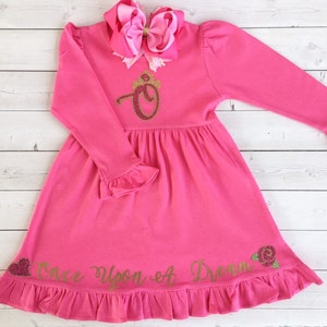 Peut inclure: Robe rose &agrave; manches longues avec une couronne dor&eacute;e paillet&eacute;e et la lettre "O" sur le devant. La robe a un ourlet et des manches &agrave; volants. Le texte "Once Upon A Dream" est &eacute;crit en paillettes dor&eacute;es sur le bas de la robe.