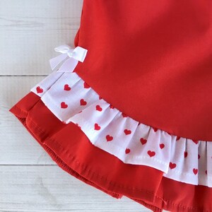 May include: Red skirt with a white ruffle trim and red heart print. The ruffle has a white background with red hearts.