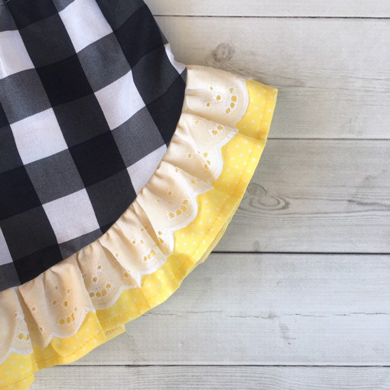 Pu&ograve; includere: Gonna in tessuto a quadri neri e bianchi con un bordo in pizzo giallo e bianco.