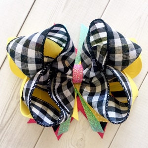 Pu&ograve; includere: Un grande fiocco per capelli a scacchi neri e bianchi con accenti di nastro giallo, verde e rosa. Il fiocco &egrave; legato con un nastro rosa scintillante al centro.