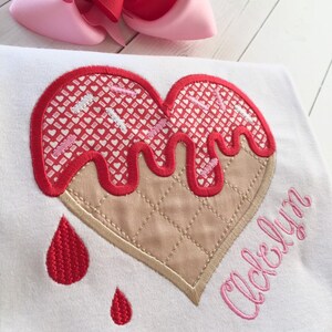 May include: A white t-shirt with a red and pink heart-shaped ice cream cone design. The ice cream is dripping and has pink sprinkles. The name "Acloelyn" is embroidered in pink below the ice cream.