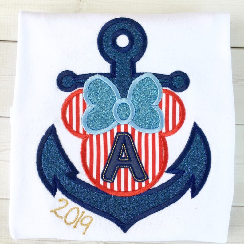 May include: A blue and red anchor with a white and red striped Minnie Mouse head with a blue bow and the letter A in the center. The year 2019 is written in gold below the anchor.