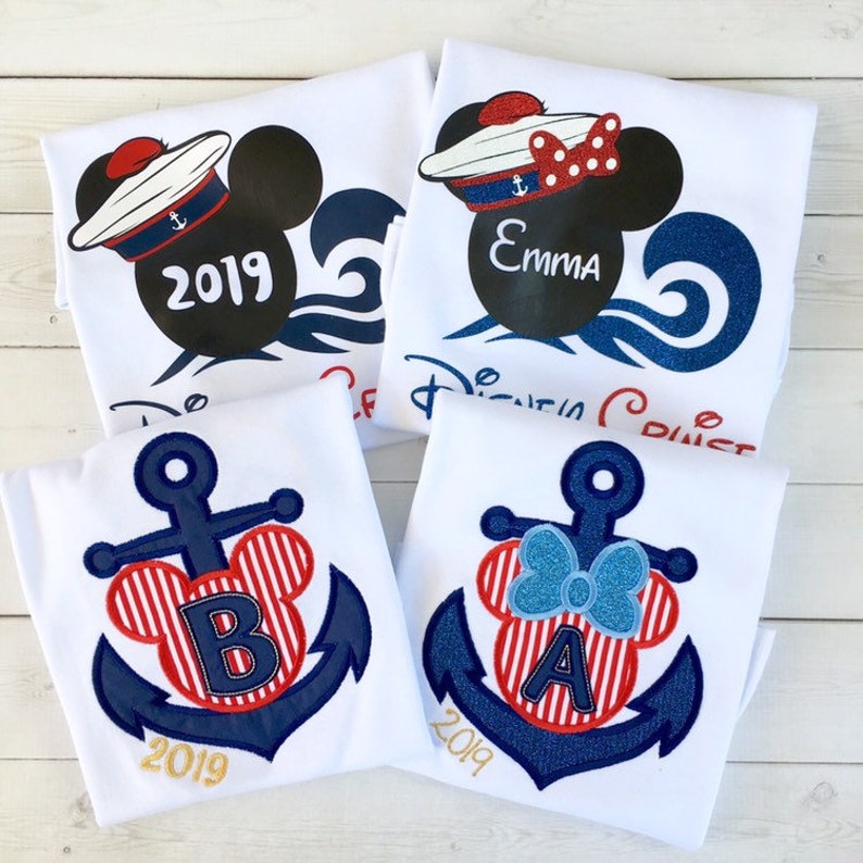 May include: Four white t-shirts with embroidered nautical-themed Disney characters. Two shirts feature Mickey Mouse and Minnie Mouse wearing sailor hats with the year 2019. The other two shirts feature Mickey Mouse and Minnie Mouse heads with anchors and the letters A and B.