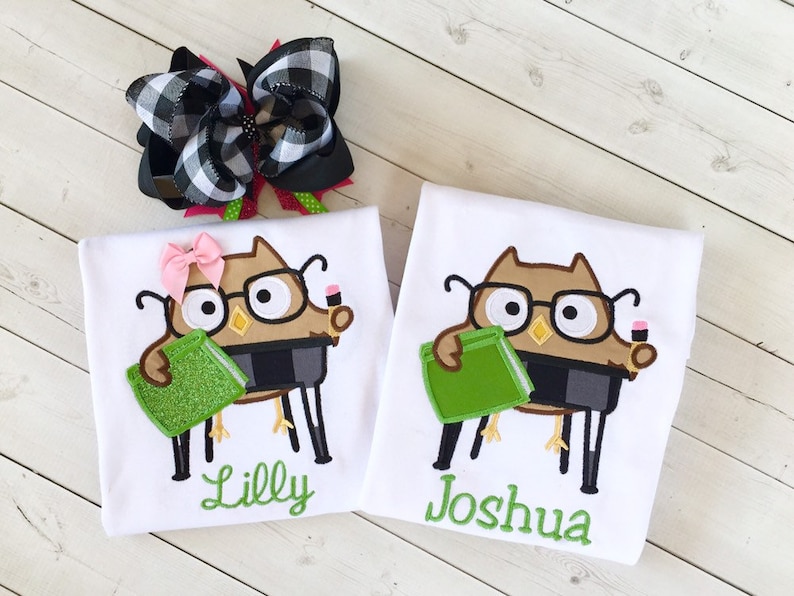 May include: Two white t-shirts with an owl design holding a book and a pencil. The shirts are personalized with the names "Lilly" and "Joshua".