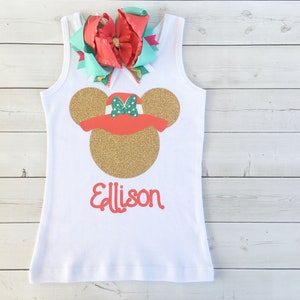 K&ouml;nnte beinhalten: Ein wei&szlig;es Tanktop mit einem goldenen Glitzer-Minnie-Maus-Kopf, der einen roten Hut mit gr&uuml;nen Punkten tr&auml;gt. Der Name "Allison" ist in Rot unter dem Minnie-Maus-Kopf geschrieben.