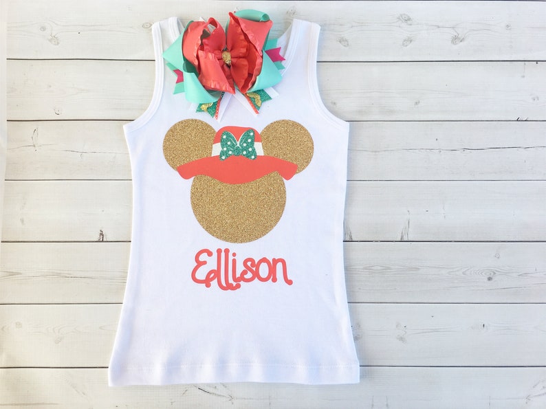 K&ouml;nnte beinhalten: Ein wei&szlig;es Tanktop mit einem goldenen Glitzer-Minnie-Maus-Kopf, der einen roten Hut mit gr&uuml;nen Punkten tr&auml;gt. Der Name "Allison" ist in Rot unter dem Minnie-Maus-Kopf geschrieben.