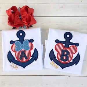 May include: Two white t-shirts with a blue anchor and red and white striped Mickey Mouse ears with a letter A and B in the middle. The year 2019 is written below the anchor.