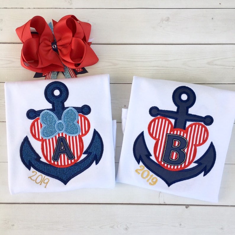 May include: Two white t-shirts with a blue anchor and red and white striped Mickey Mouse ears with a letter A and B in the middle. The year 2019 is written below the anchor.
