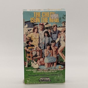 May include: A VHS tape for the movie "The Check Is in the Mail." The cover features a group of people, a pig, and a duck. The text on the cover reads "Plastic Money, Phony Credit, Enough is Enough! This American Family Has Had It!" Starring Brian Dennehy and Anne Archer.