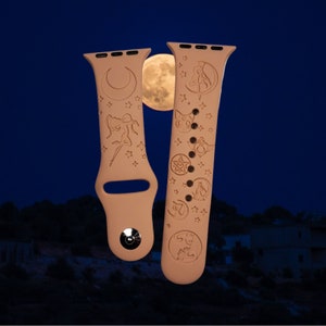 Pode incluir: Duas pulseiras marrons para Apple Watch com um design de lua e estrelas. Uma pulseira apresenta uma silhueta de uma mulher com uma lua crescente e estrelas. A outra pulseira apresenta uma lua crescente, estrelas e uma silhueta de gato.