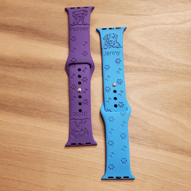 May include: Two personalized Apple Watch bands with dog paw prints. The purple band has the name "Bobo" and a dog's face. The blue band has the name "Jenny" and a dog's face.