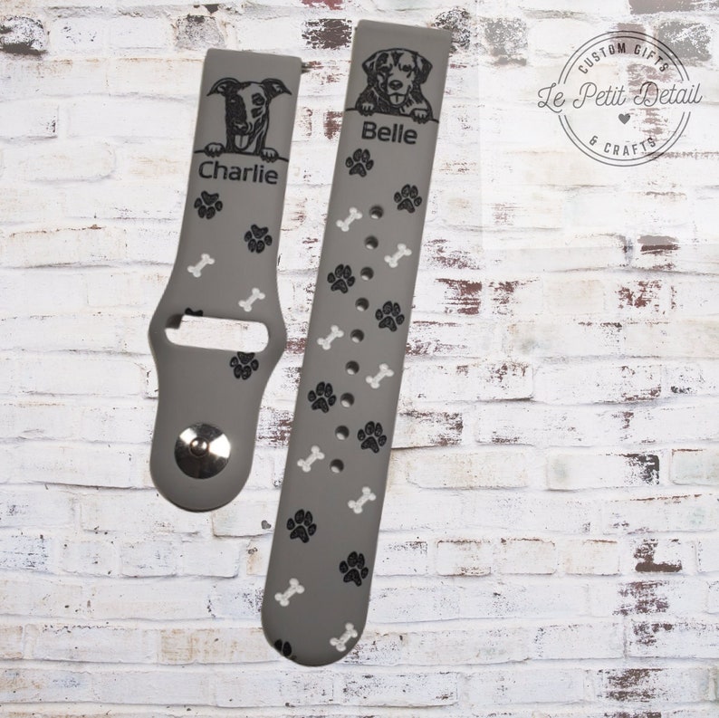 May include: Two gray silicone watch bands with paw print and bone designs. The bands are personalized with the names "Charlie" and "Belle" and feature images of dogs.