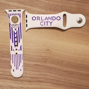 Pode incluir: Banda branca para Apple Watch com um padr&atilde;o de listras brancas e roxas e uma banda branca com o texto "ORLANDO CITY" em roxo. A banda apresenta um logotipo de le&atilde;o com o texto "ORLANDO CITY" abaixo.