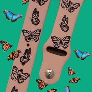 May include: A pink Apple Watch band with a black butterfly design. The band is shown with several orange and blue butterflies scattered around it.