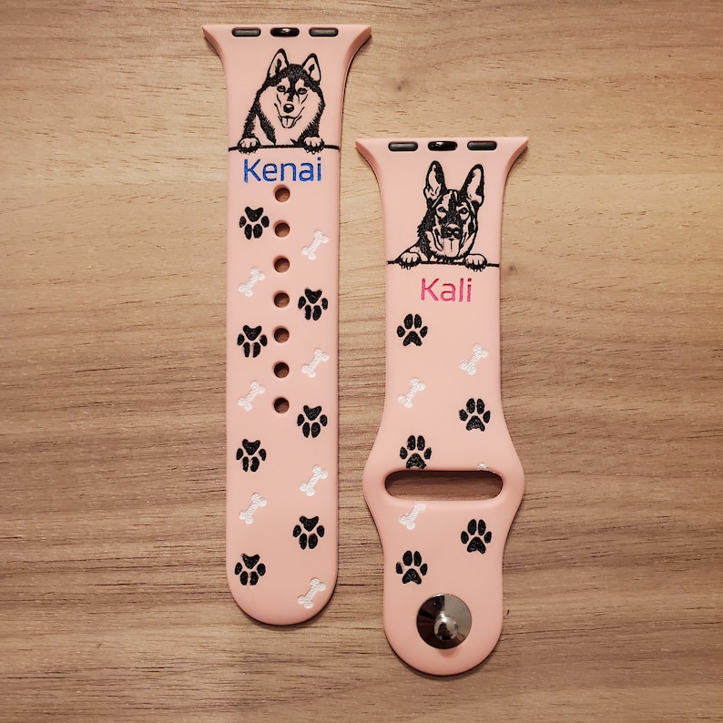 May include: Two pink Apple Watch bands with paw print and bone designs. The band on the left has a black and white husky dog image and the text "Kenai". The band on the right has a black and white German Shepherd dog image and the text "Kali".