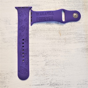 Pode incluir: Pulseira de silicone roxa para Apple Watch com um design Wakanda Forever. A pulseira apresenta um padr&atilde;o repetido de m&aacute;scaras do Pantera Negra.