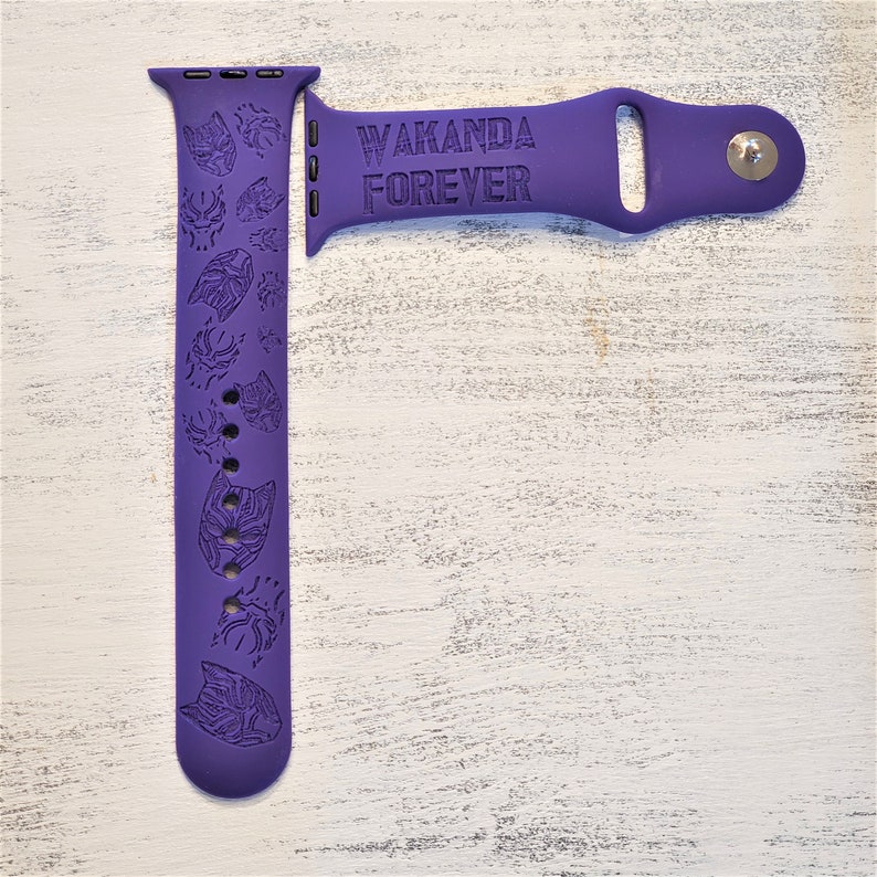 Pode incluir: Pulseira de silicone roxa para Apple Watch com um design Wakanda Forever. A pulseira apresenta um padr&atilde;o repetido de m&aacute;scaras do Pantera Negra.