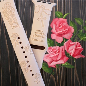 May include: A white Apple Watch band with a religious design. The band features a cross, rosary beads, and the text "Estoy contigo siempre Katherine".