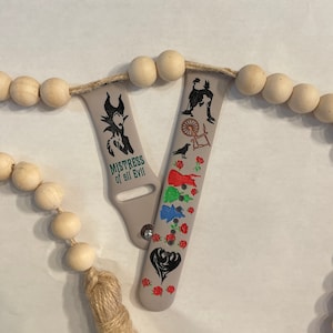 May include: Two gray watch bands with a black and white design. One band features a silhouette of Maleficent from Disney's Sleeping Beauty with the text "Mistress of all Evil". The other band features a silhouette of Cinderella and other characters from the movie.