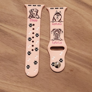 May include: Two pink Apple Watch bands with black paw prints and white bone designs. The bands have personalized engravings with dog names and the text "Dixie", "Kofuku", and "Lyla Lu".