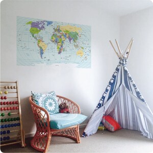Peut inclure: Un mur blanc avec un autocollant de carte du monde, un tipi rayé bleu et blanc, un fauteuil en osier avec un coussin turquoise et un ours en peluche, et un boulier en bois.
