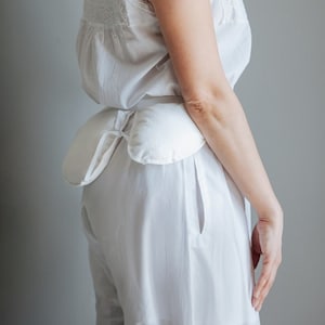 Puede incluir: Un camisón blanco de algodón de manga larga con ribete de encaje y un cinturón de tela blanco. El camisón tiene una cintura fruncida y un corte holgado.