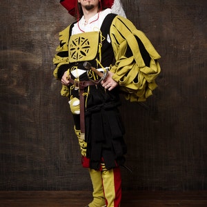 May include: A person in a Renaissance-style costume. The outfit features a large red hat, a yellow and black doublet, and black breeches. A sword hangs at the waist. The costume includes yellow and red leggings and black shoes. The background is a dark wood.
