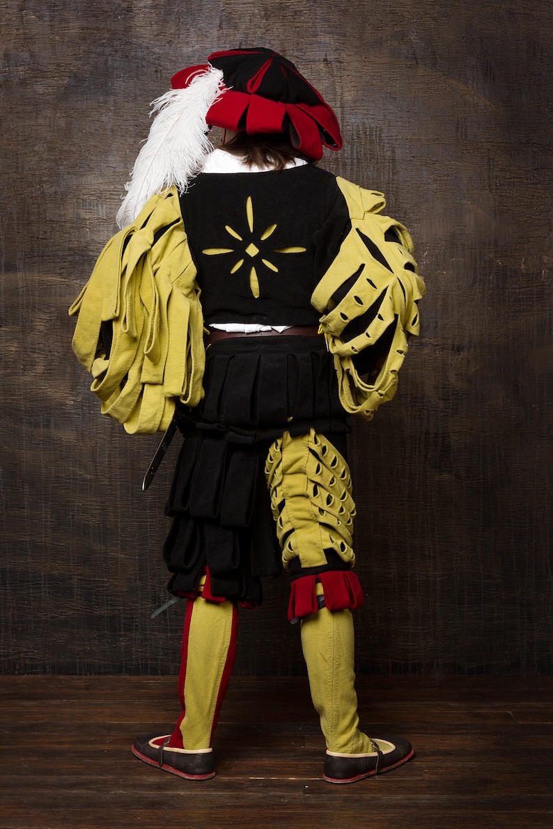 May include: A historical costume featuring a black and yellow doublet with a starburst design, black shorts, and yellow leggings with red accents. The outfit includes a red and black hat with a white feather and black shoes.