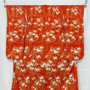 May include: A vibrant red kimono with a floral pattern. The fabric is adorned with white flowers, green leaves, and small birds. The kimono is displayed open, showcasing its full design and flowing sleeves.