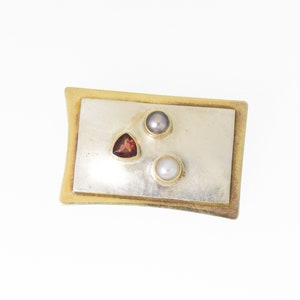 Pode incluir: Um broche retangular de ouro e prata com tr&ecirc;s pedras preciosas. O broche tem uma pedra preciosa triangular vermelha e duas pedras preciosas redondas brancas.