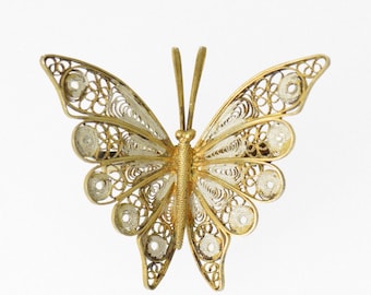 May include: A gold butterfly brooch crafted from filigree wire. The wings are intricately detailed and have a delicate, airy appearance.