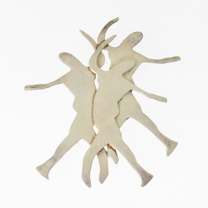 May include: Silver pendant featuring a stylized design of three figures dancing, with their bodies overlapping and intertwined.