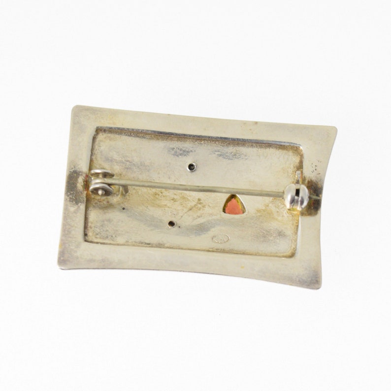 Pode incluir: Broche prateada com uma moldura retangular e uma pedra rosa no centro. A parte de tr&aacute;s da broche tem um pino e um fecho.