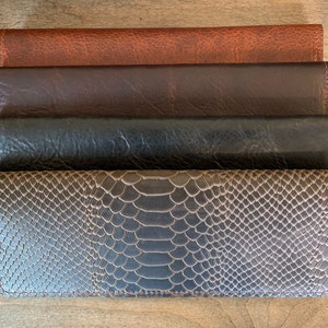 May include: Four leather wallets in different colors and textures. The top wallet is brown, the second is dark brown, the third is black, and the bottom wallet is a snakeskin pattern.