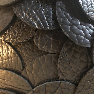 May include: Close-up of a black leather surface made of overlapping, circular pieces. The leather has a textured, pebbled appearance.