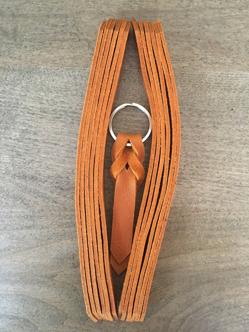 Puede incluir: Un llavero de cuero marr&oacute;n con un nudo trenzado y un anillo de llave plateado.