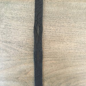Puede incluir: Una correa de cuero negra con un extremo puntiagudo. El cuero tiene un aspecto desgastado con grietas y un ligero brillo.