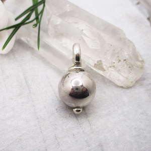 Puede incluir: Un amuleto de plata en forma de esfera con un pequeño bucle en la parte superior.
