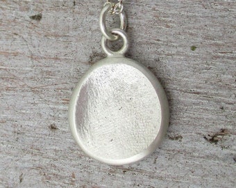 May include: A silver pendant necklace with a round, smooth, silver disc charm. The pendant is hanging from a silver chain.