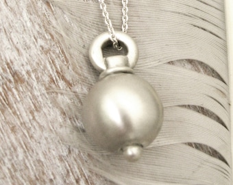 May include: A silver necklace with a round pendant. The pendant is smooth and has a slight shine. The necklace is on a white feather.