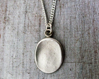 May include: A silver necklace with a round pendant featuring a detailed fingerprint design.