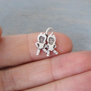 May include: Silver charm featuring two stylized figures of children holding hands. The charm has a loop for attaching to a bracelet or necklace.