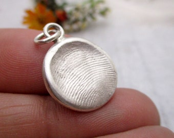 May include: A silver round pendant with a fingerprint design. The pendant has a loop at the top for attaching to a chain.