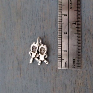 May include: Silver charm featuring two stylized figures holding hands, approximately 1 inch in size.